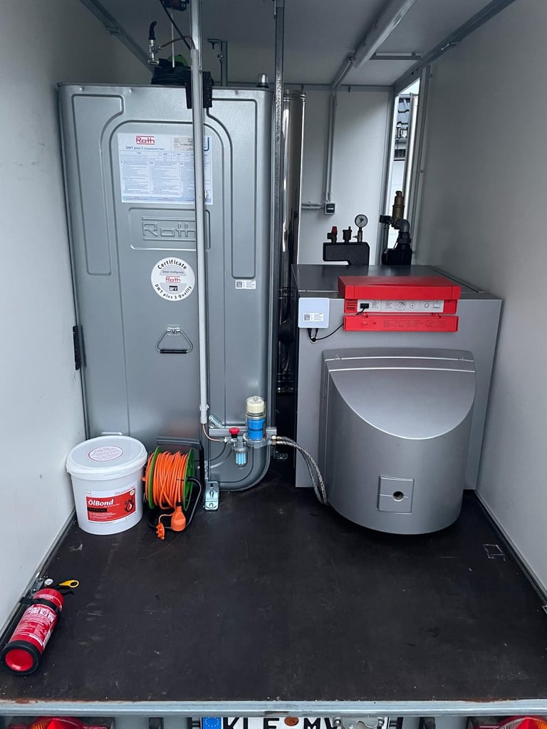 Interior of a utility trailer containing HVAC equipment, a red metal cabinet, water softener, electrical supplies, and various tools on a black floor