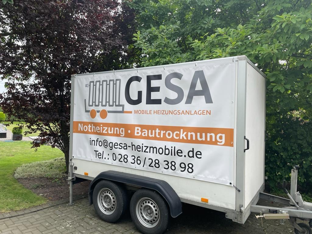 White GESA mobile heating trailer with Notheizung and Bautrocknung services, parked against green trees