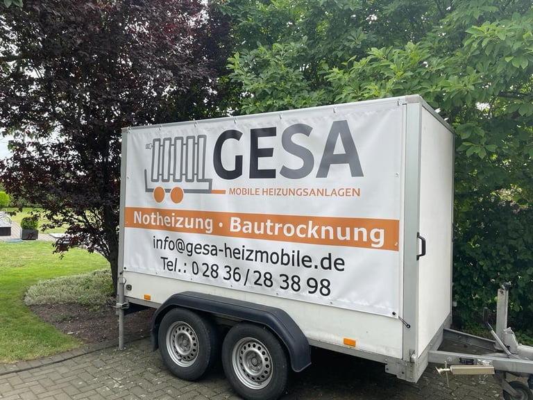 White GESA mobile heating trailer with Notheizung and Bautrocknung services, parked against green trees