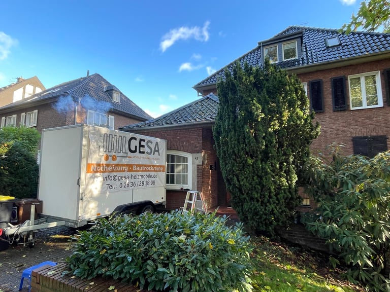 White GESA service truck parked beside a brick residential house with ivy-covered walls under blue sky